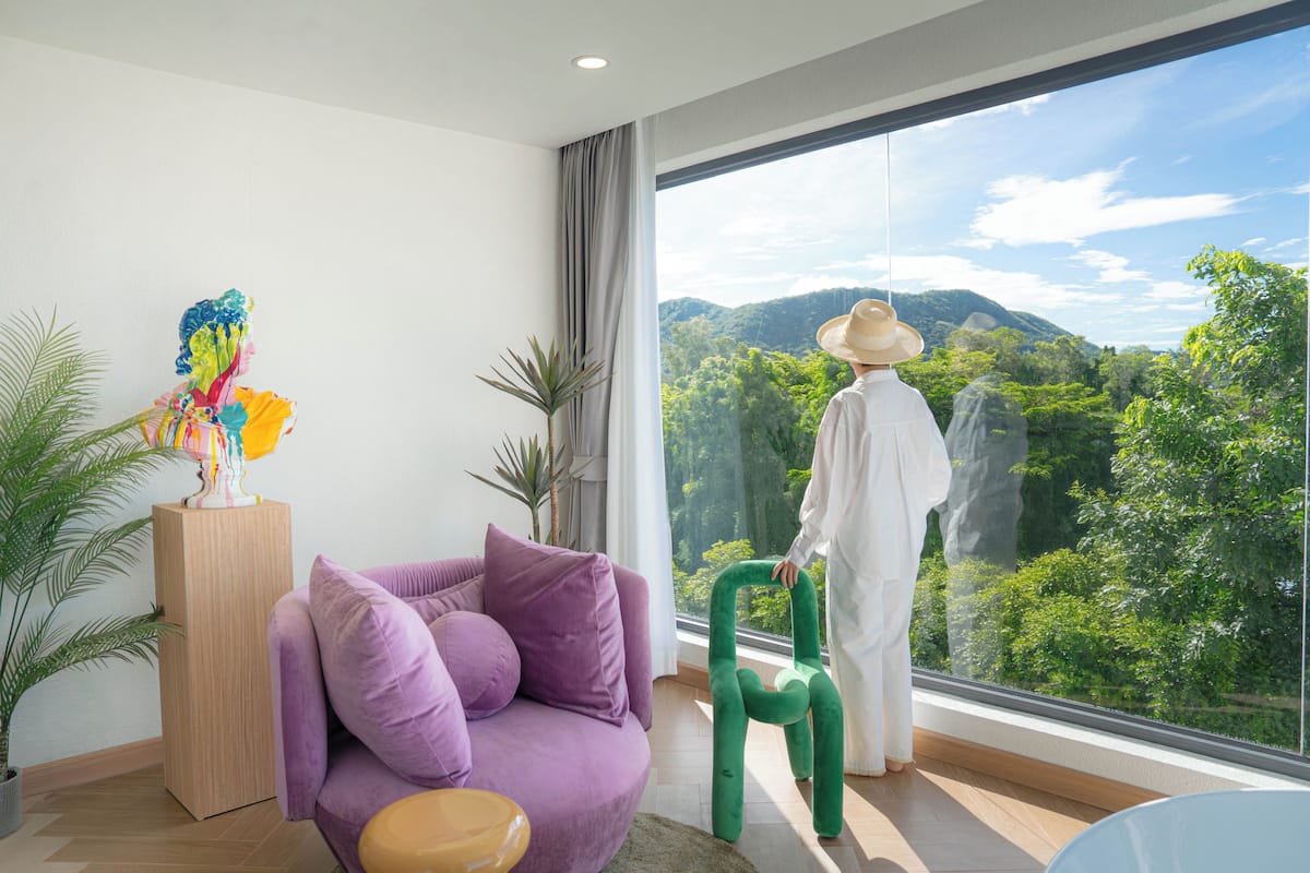 A modern living room with a purple sofa, a green chair, and a large window offering a view of a mountainous landscape.