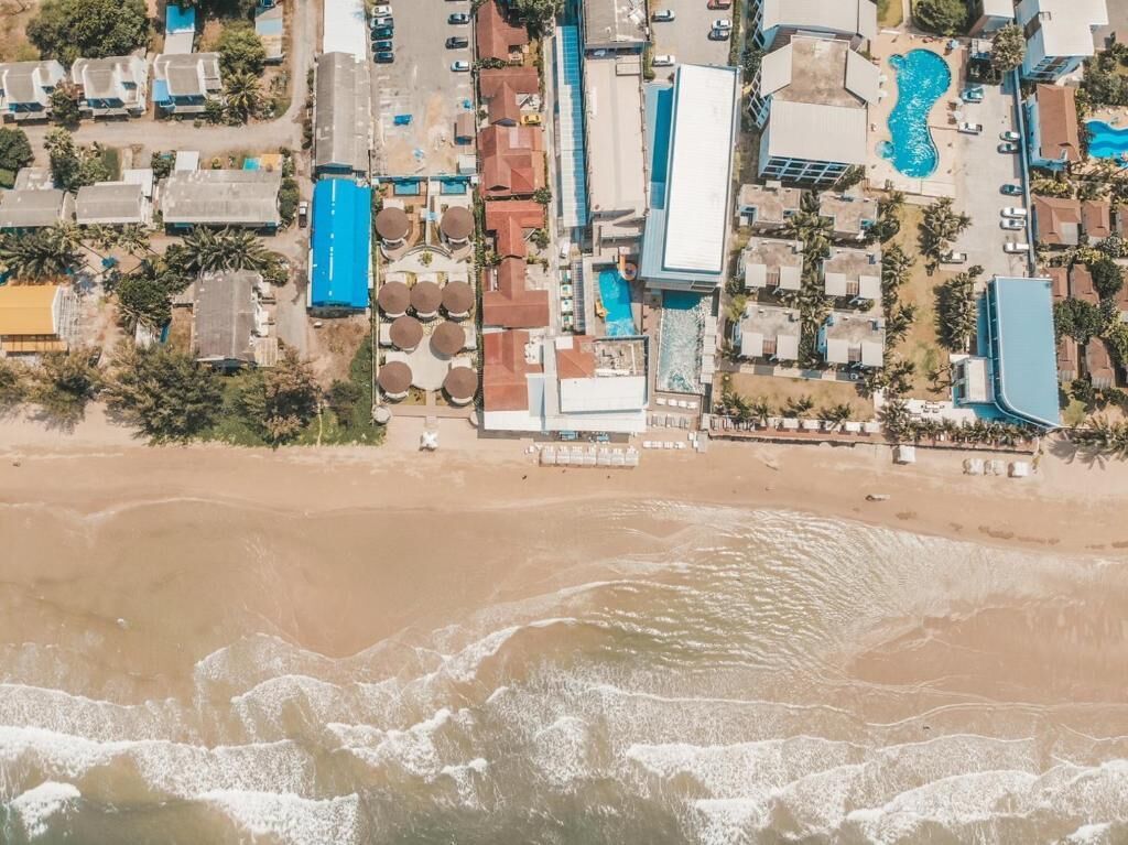An aerial view of a coastal hotel with multiple buildings, a beach, and a swimming pool.