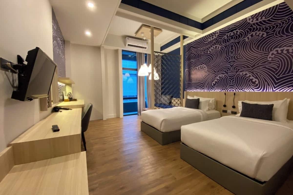 A hotel room with a desk, two beds, a TV, and a patterned wall.