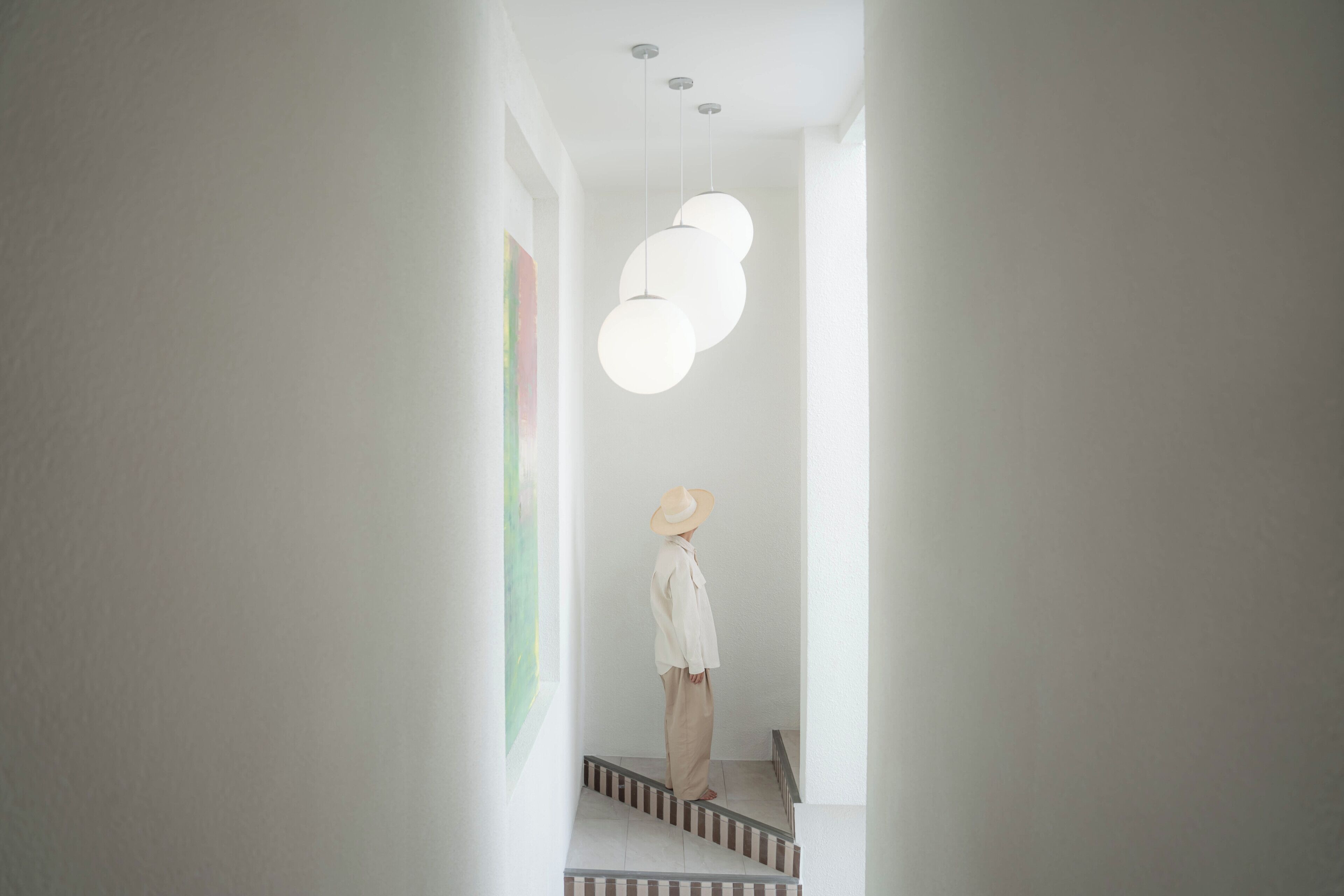 A person standing on a staircase in a well-lit hallway with a modern pendant light fixture.