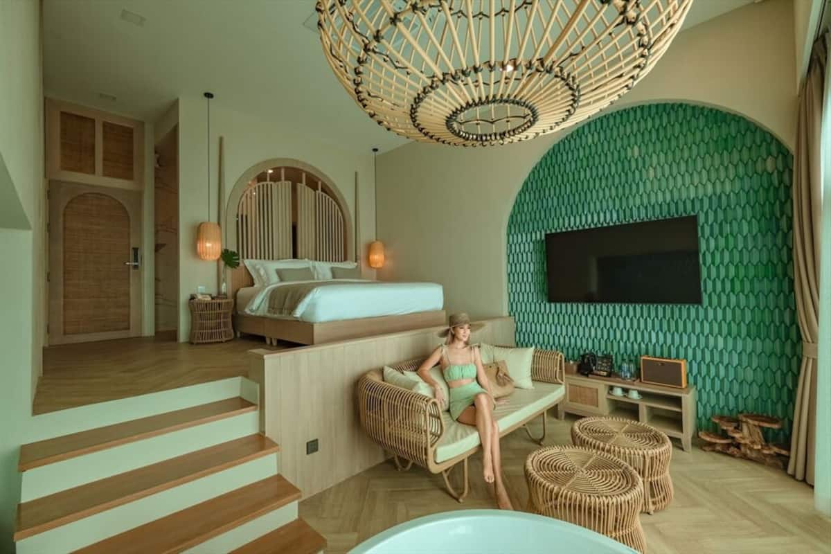 A modern bedroom with a bed, a TV, and a seating area with a wicker sofa and ottomans.