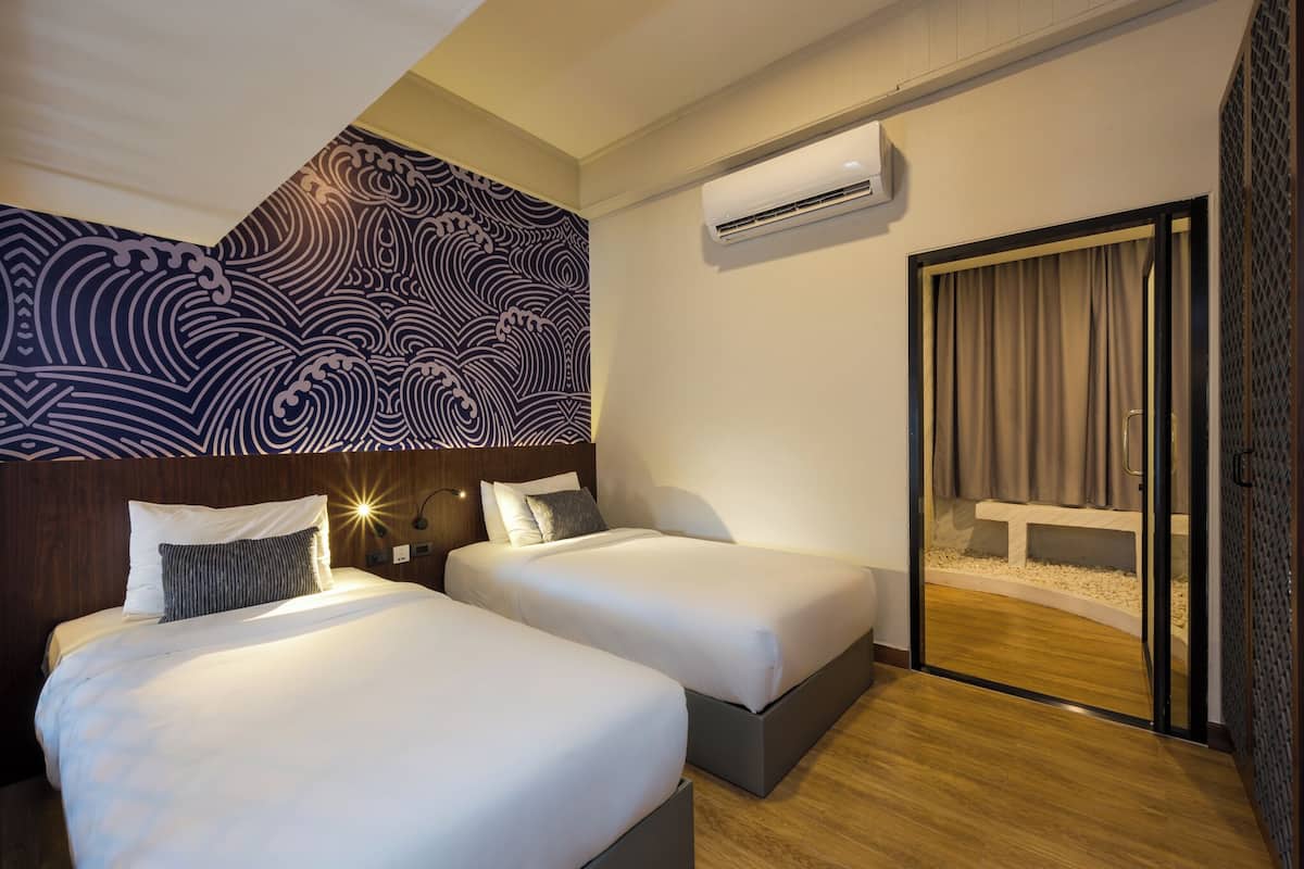 A hotel room with two beds, a patterned wall, an air conditioning unit, and a sliding glass door leading to a balcony.