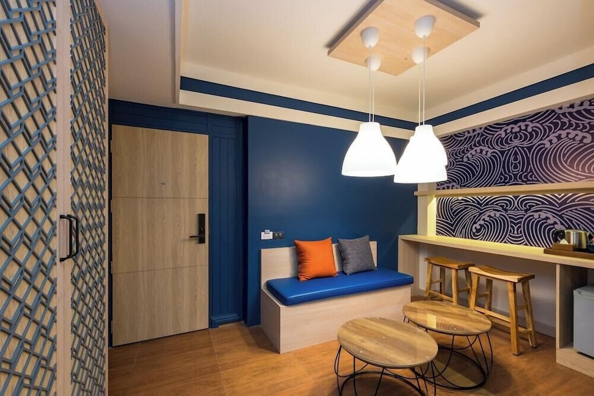 A modern room with a blue accent wall, a wooden bench with cushions, a hanging light fixture, and a patterned wall.