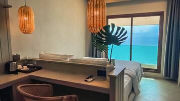 A hotel room with a bed, a desk with a chair, a large window with a view of the sea, and two hanging wicker lamps.