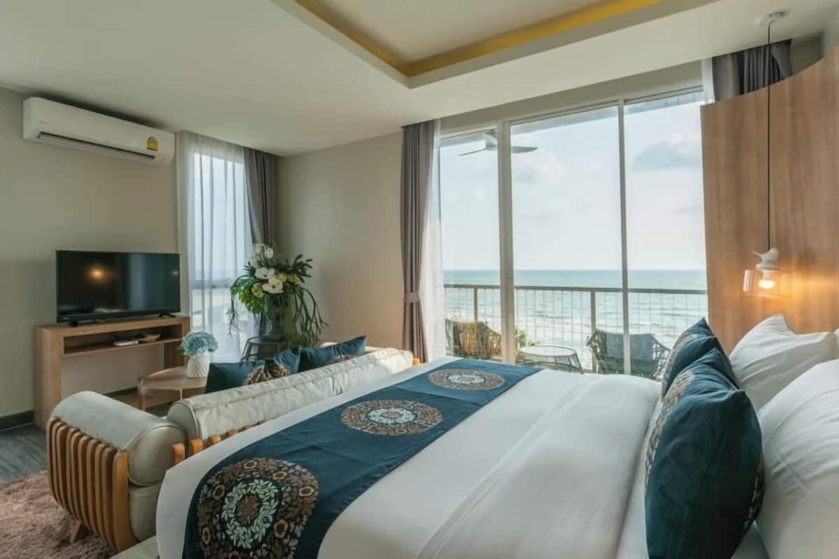 A hotel room with a large bed, a TV, a balcony with a view of the sea, and a plant on the windowsill.