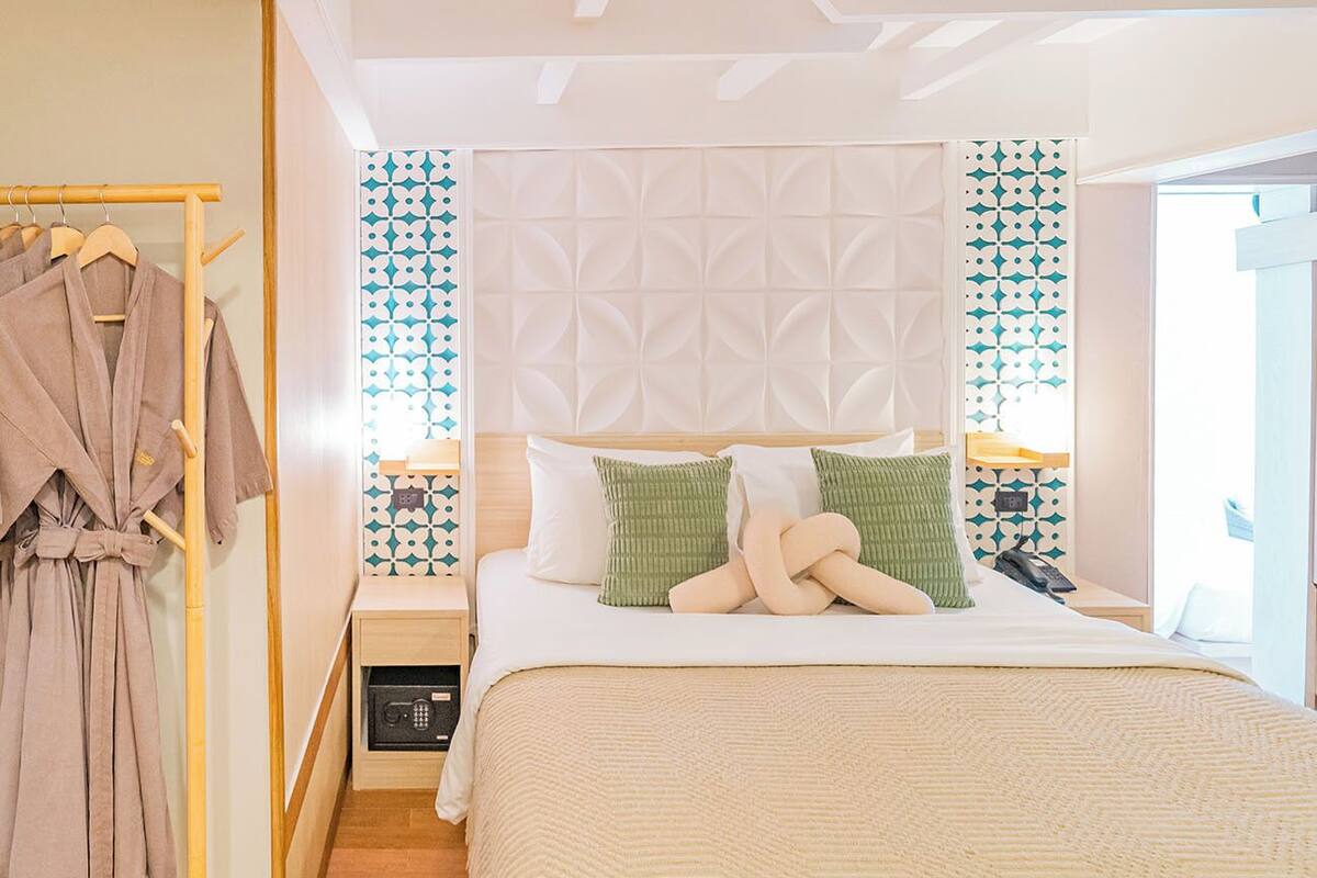 A bedroom with a bed, a bedside table, a nightstand, a wall-mounted radio, and a clothing rack.