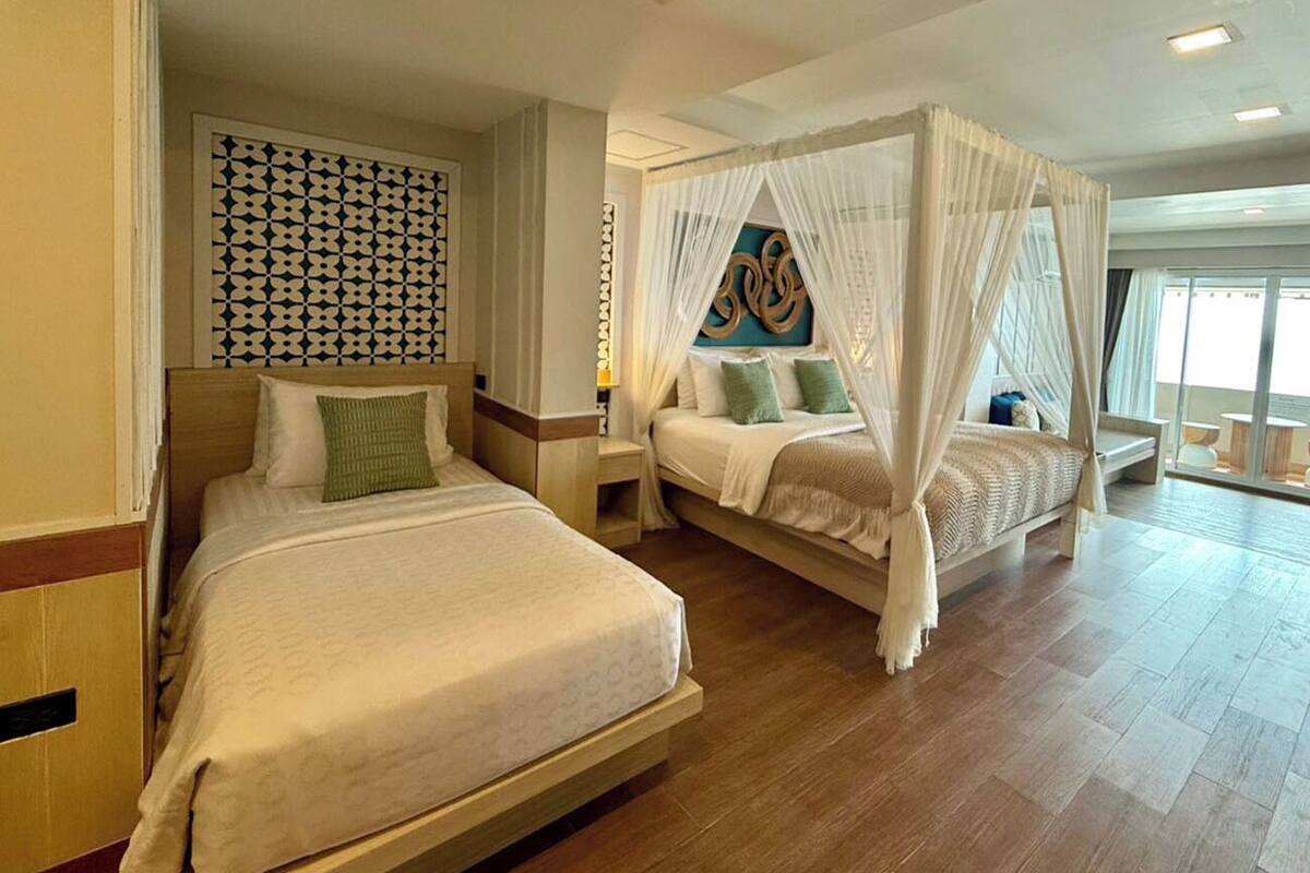 A hotel room with two beds, a patterned wall, a large window, and a ceiling with recessed lighting.