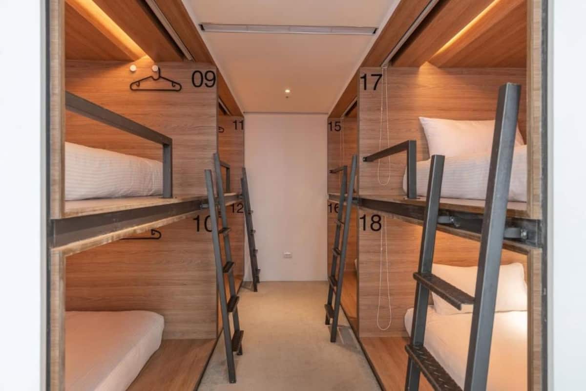 A narrow corridor with bunk beds labeled with numbers, wooden walls, and a carpeted floor.