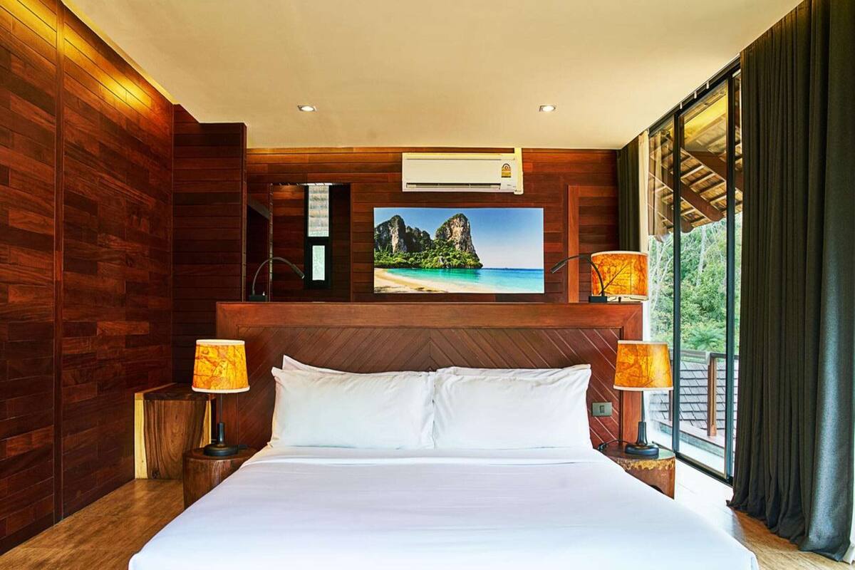 A hotel room with a large bed, wooden walls, a painting of a beach, and two lamps.