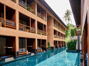 Un hotel con varios balcones, piscina y abundante vegetación.