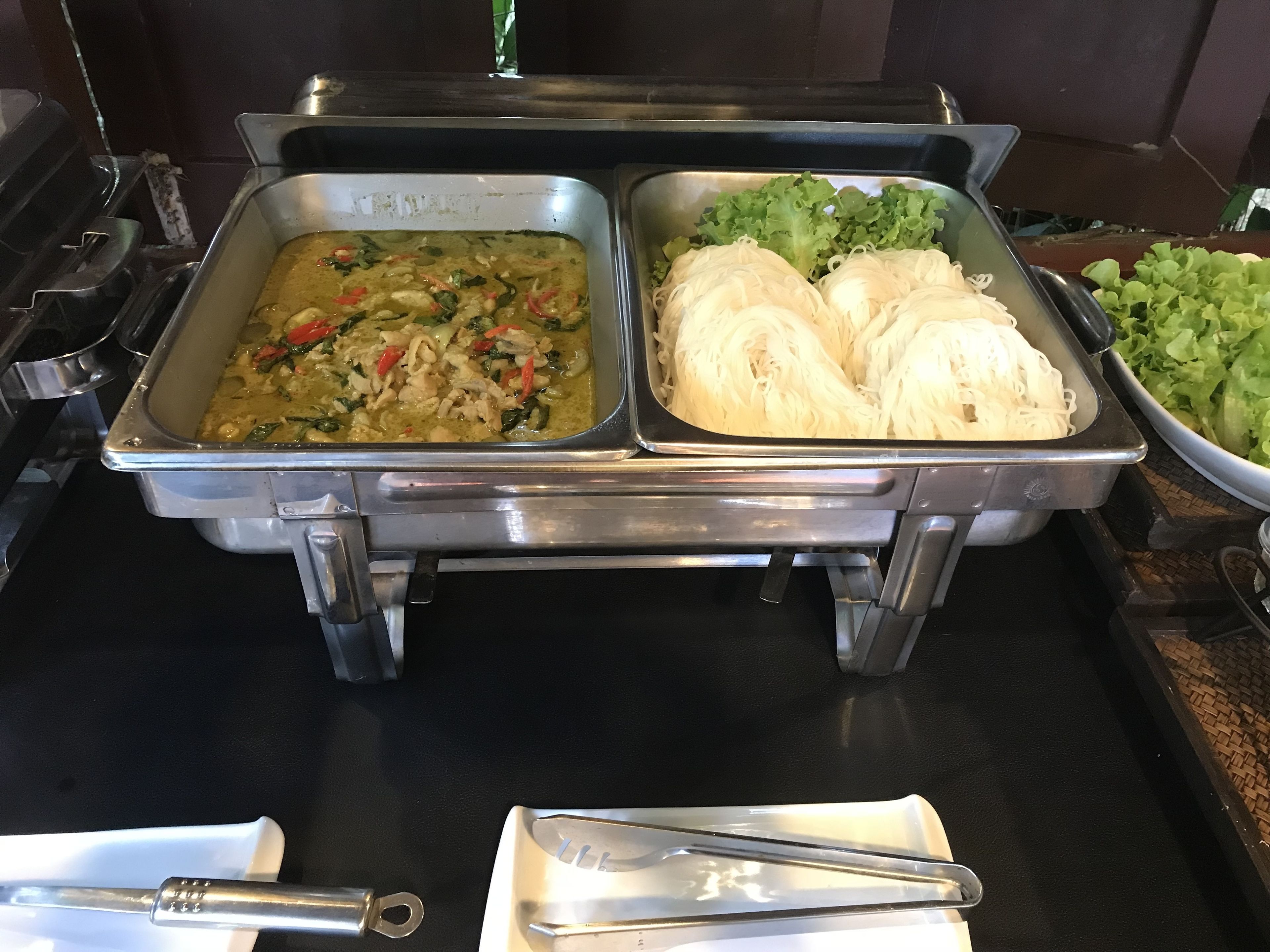 A buffet with two trays of food, one containing a noodle dish and the other a salad.