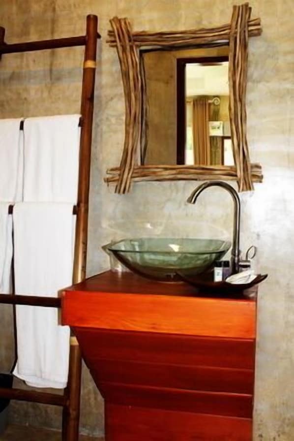 Un baño con tocador de madera, lavabo de vidrio y espejo con marco rústico.