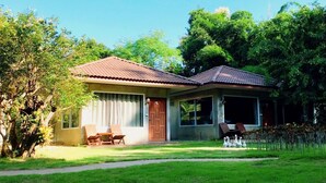 A two-story house with a tiled roof, a front porch with a table and chairs, and a small garden area with a pathway leading to the house.