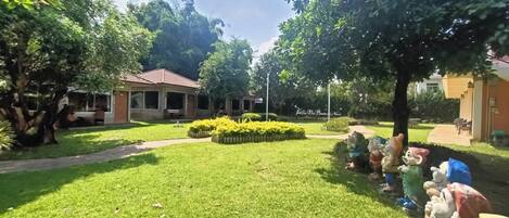A well-maintained garden with a lawn, trees, and a pathway leading to a building with a red roof.