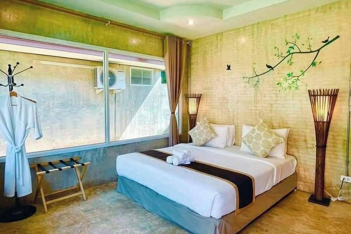 Un dormitorio con una cama grande, una ventana con cortinas, un ventilador de pie y un adorno en la pared.