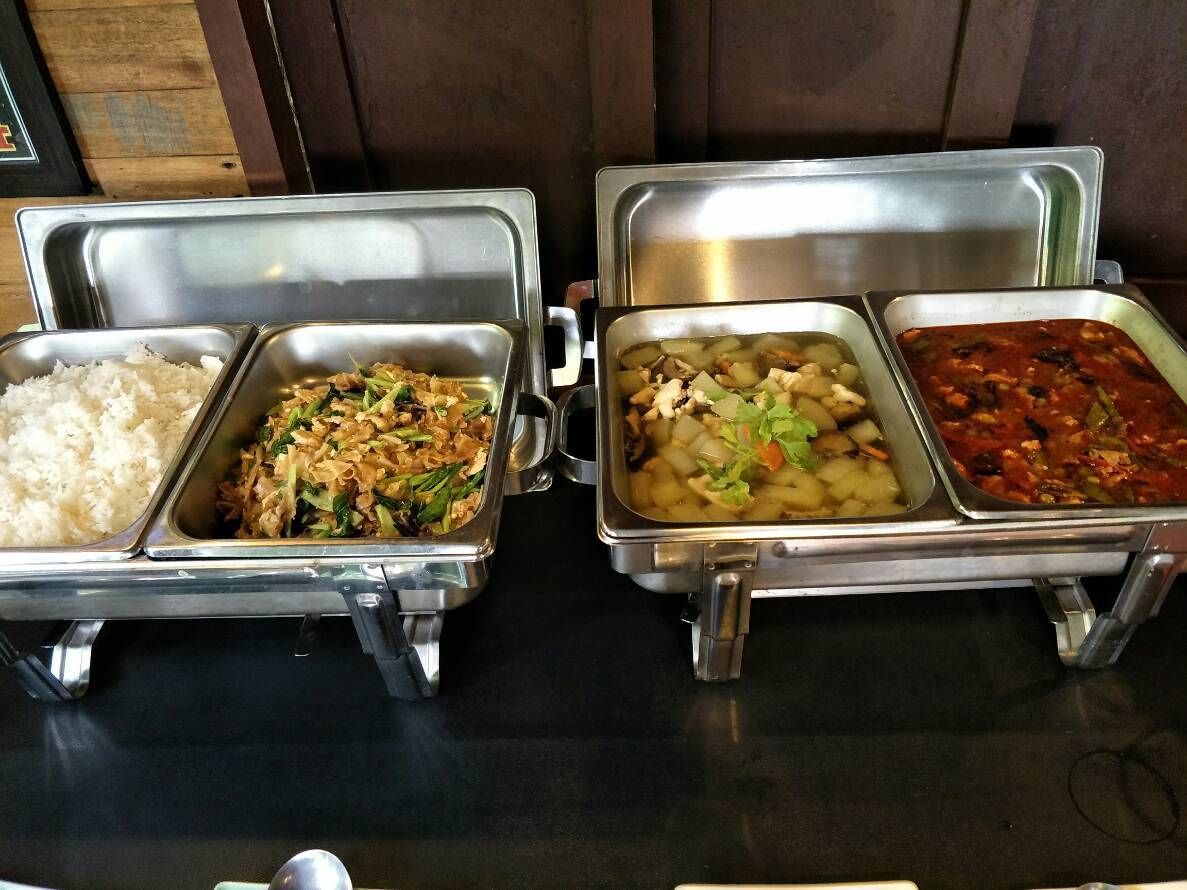 A buffet with three metal trays containing rice, stir-fried vegetables, and a vegetable stew.