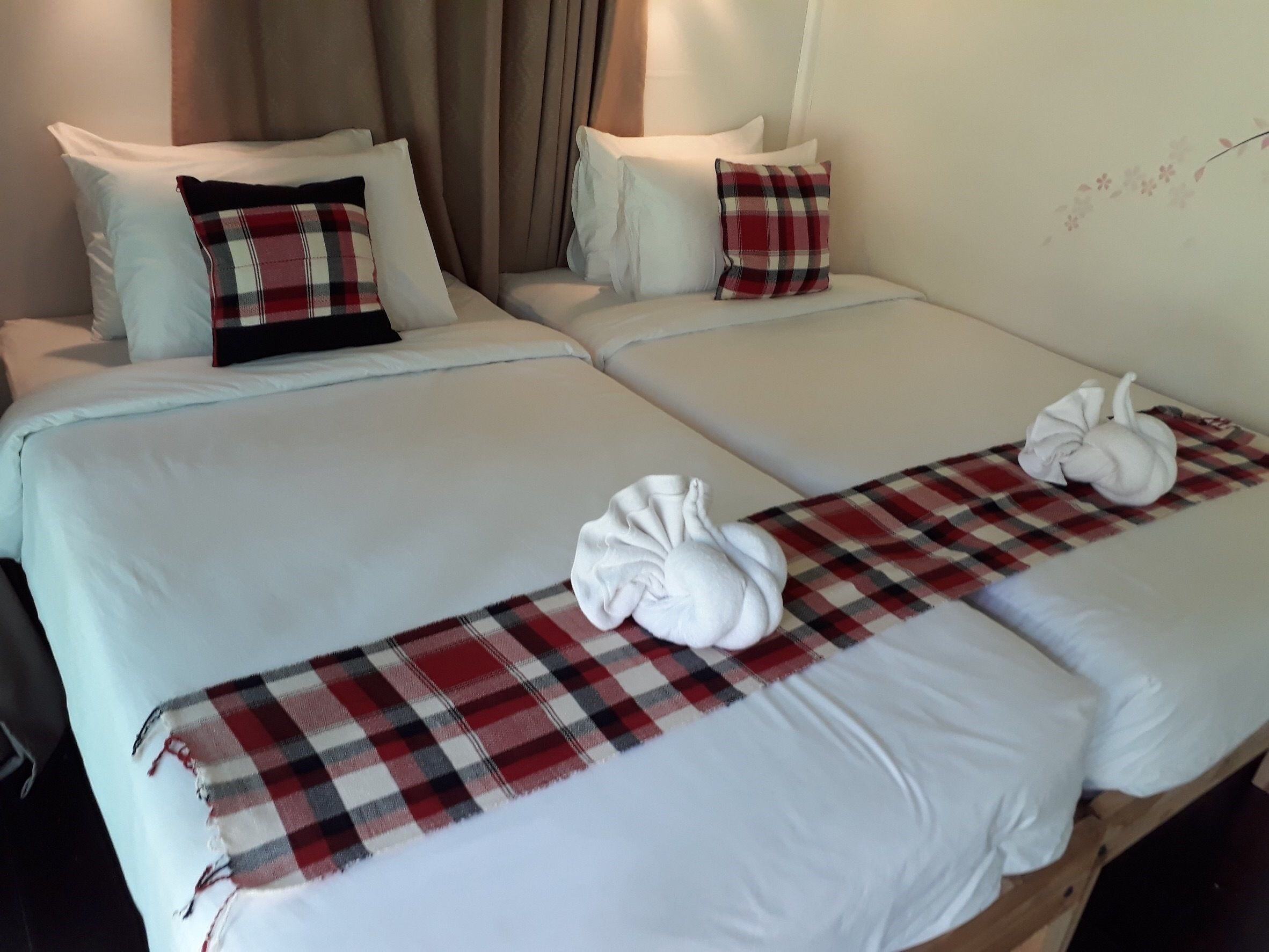 Une chambre d’hôtel avec deux lits, chacun recouvert d’une literie blanche et d’une couverture à carreaux rouges et noirs. Il y a deux oreillers, l’un à carreaux rouges et noirs et l’autre uni, blanc.