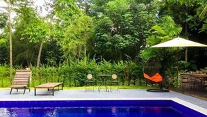 A swimming pool with a wooden deck, two tables, and a hanging chair.