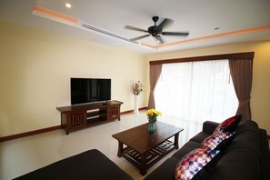 A living room with a flat-screen TV, a wooden coffee table, a sofa, and a ceiling fan. - Bang Saray Pool Villa by Pattaya Sunny Rentals (Sattahip)