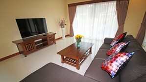 A living room with a flat-screen TV, wooden coffee table, sofa with patterned cushions, and a vase with flowers. - Bang Saray Pool Villa by Pattaya Sunny Rentals (Sattahip)