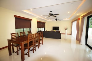 A spacious living area with a dining table and chairs, a sofa, a TV, and a ceiling fan. - Bang Saray Pool Villa by Pattaya Sunny Rentals (Sattahip)
