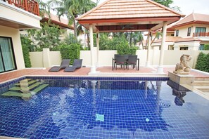 A swimming pool with tiled flooring, lounge chairs, and a covered seating area. - Bang Saray Pool Villa by Pattaya Sunny Rentals (Sattahip)
