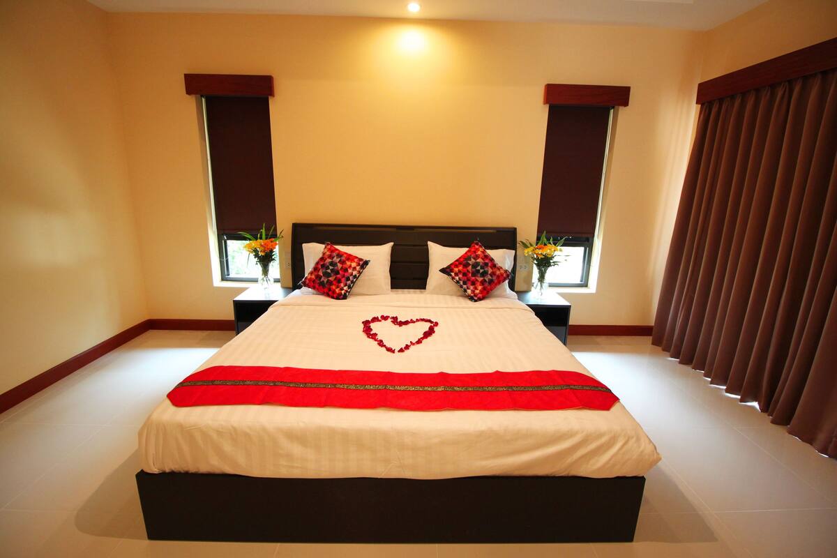 A neatly made bed with a heart-shaped decoration, two pillows with a checkered pattern, and a red decorative strip.
