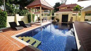A swimming pool with tiled flooring, lounge chairs, and a gazebo structure. - Bang Saray Pool Villa by Pattaya Sunny Rentals (Sattahip)
