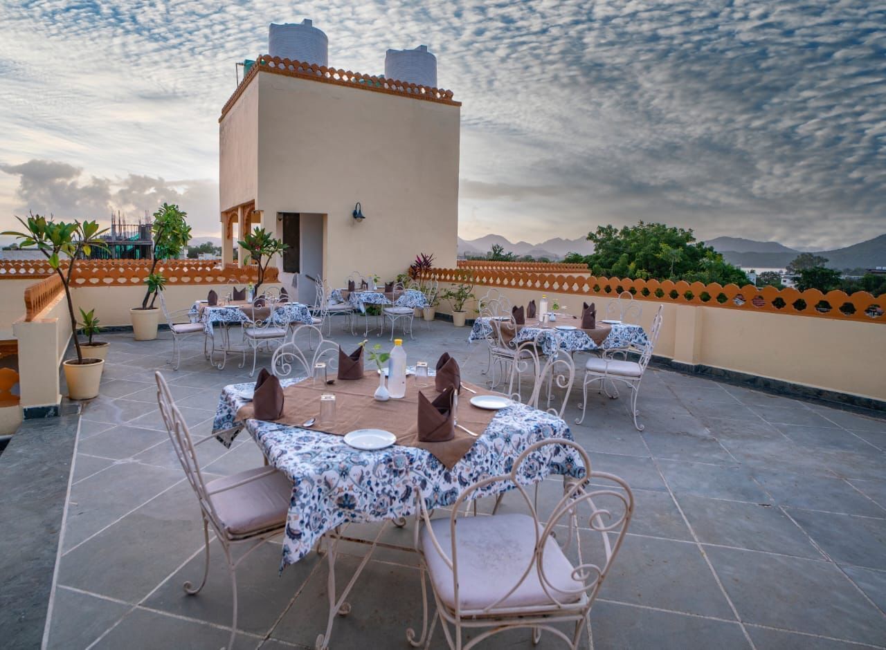 An outdoor dining area with tables and chairs, a building in the background, and a mountainous landscape.