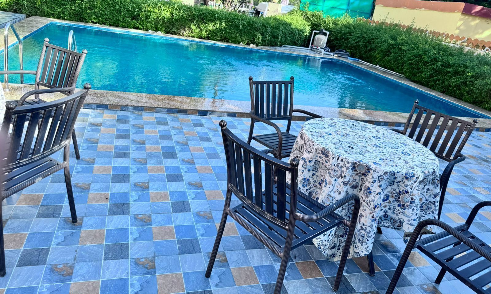 Ein Poolbereich mit Fliesenboden, einem runden Tisch mit Blumenmuster und Metallstühlen.