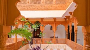 Un patio arquitectónico con suelo de tablero de ajedrez, arcos ornamentales y plantas en macetas.