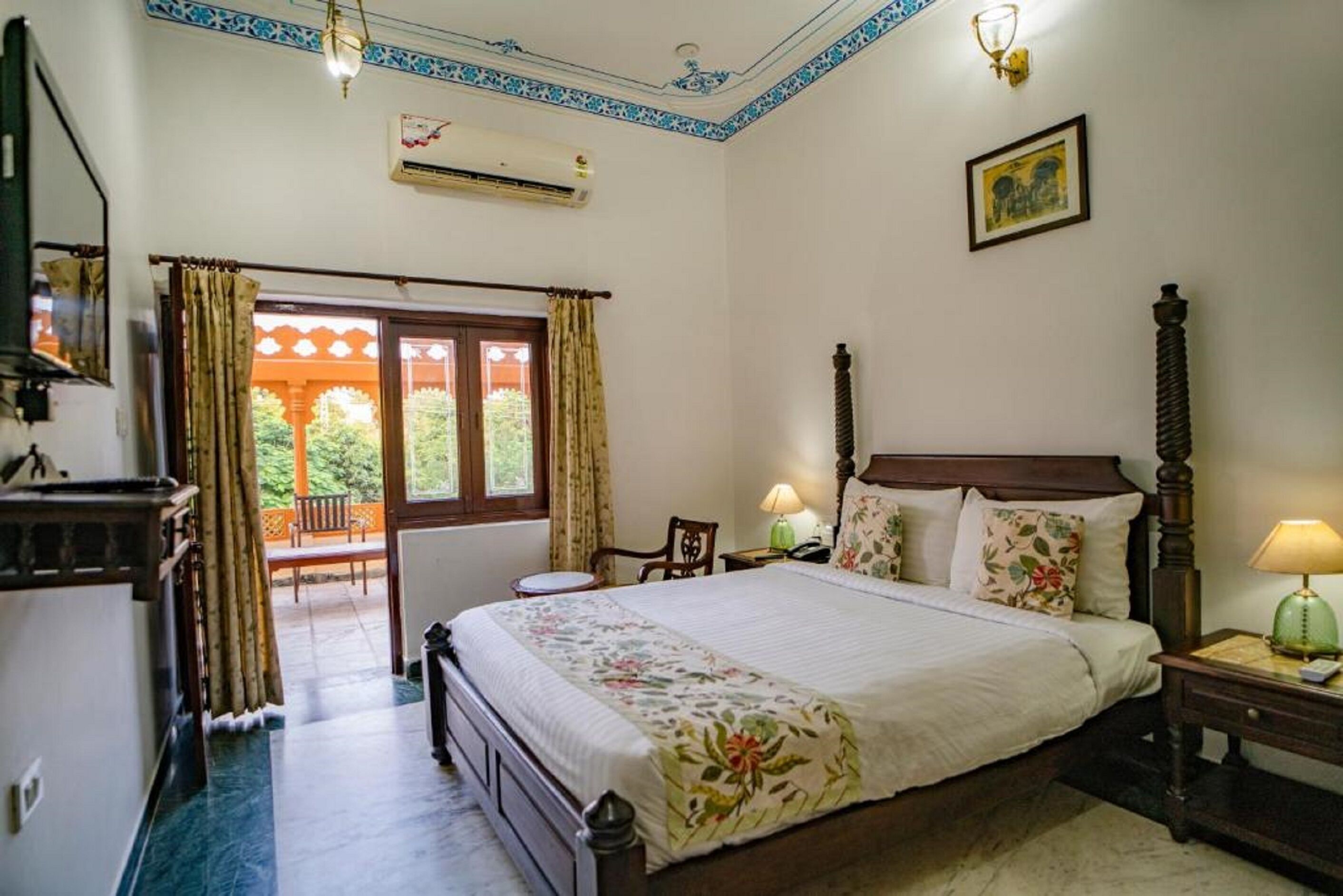 A bedroom with a large bed, a wooden headboard, a nightstand, a lamp, and a window with curtains.