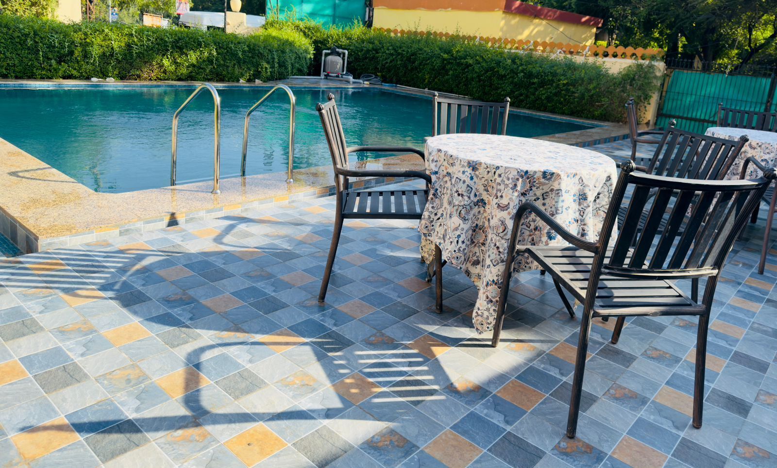 A pool area with tiled flooring, a table with chairs, and a pool with metal railings.