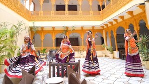 Un patio con arquitectura ornamentada, plantas en macetas y un grupo de personas vestidas con trajes tradicionales.