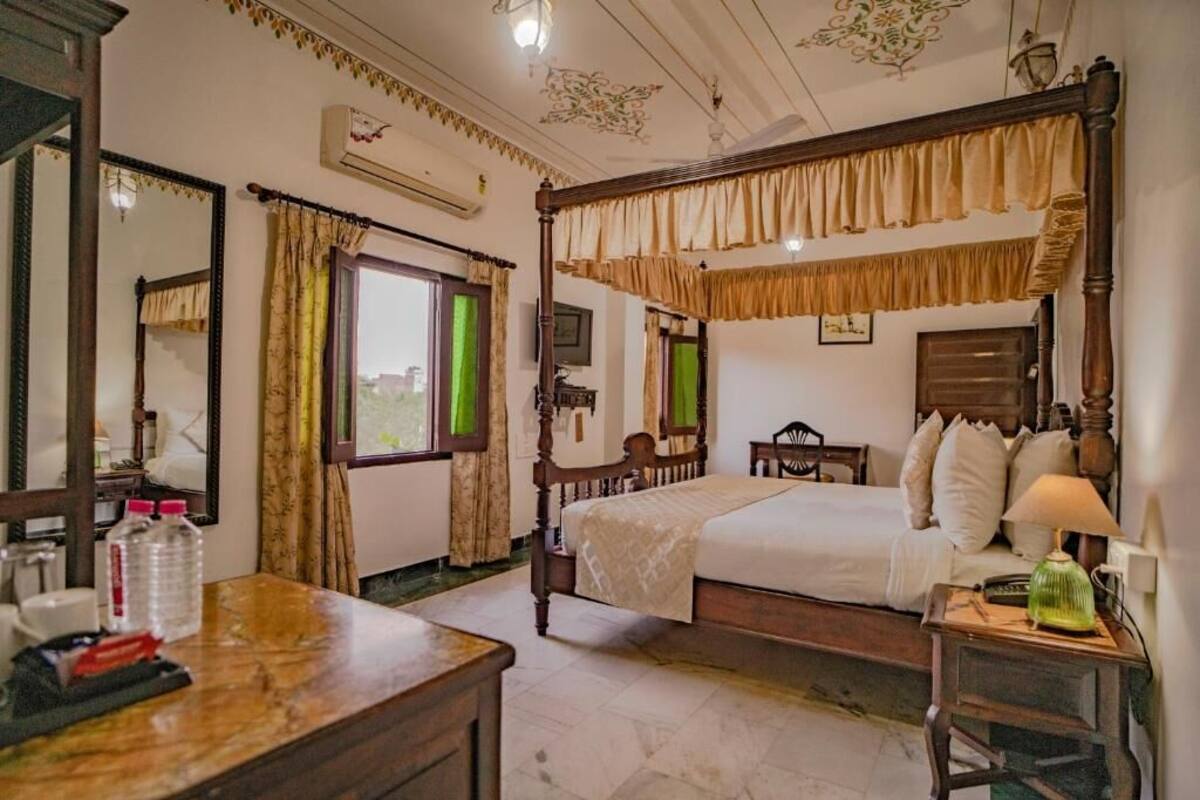 A traditional four-poster bed with a canopy, a wooden desk with a lamp, and a mirror on the wall.