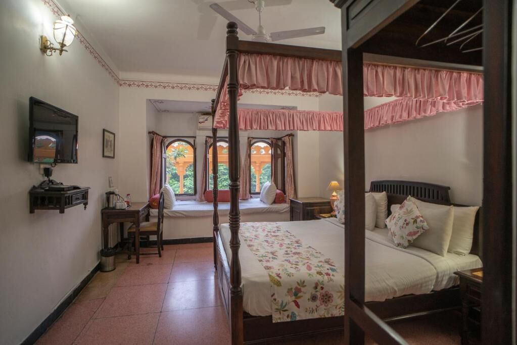 A four-poster bed with a floral bedspread, a desk with a lamp, and a television on the wall.