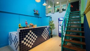 Un espace d’accueil avec un comptoir carrelé à motifs à carreaux, une plante en pot et un escalier doté de rampes de couleur turquoise.