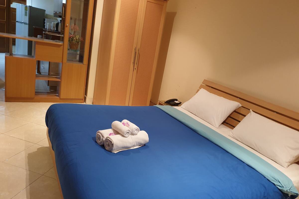 A hotel room with a large bed, a wooden wardrobe, a telephone, and a fire exit sign.