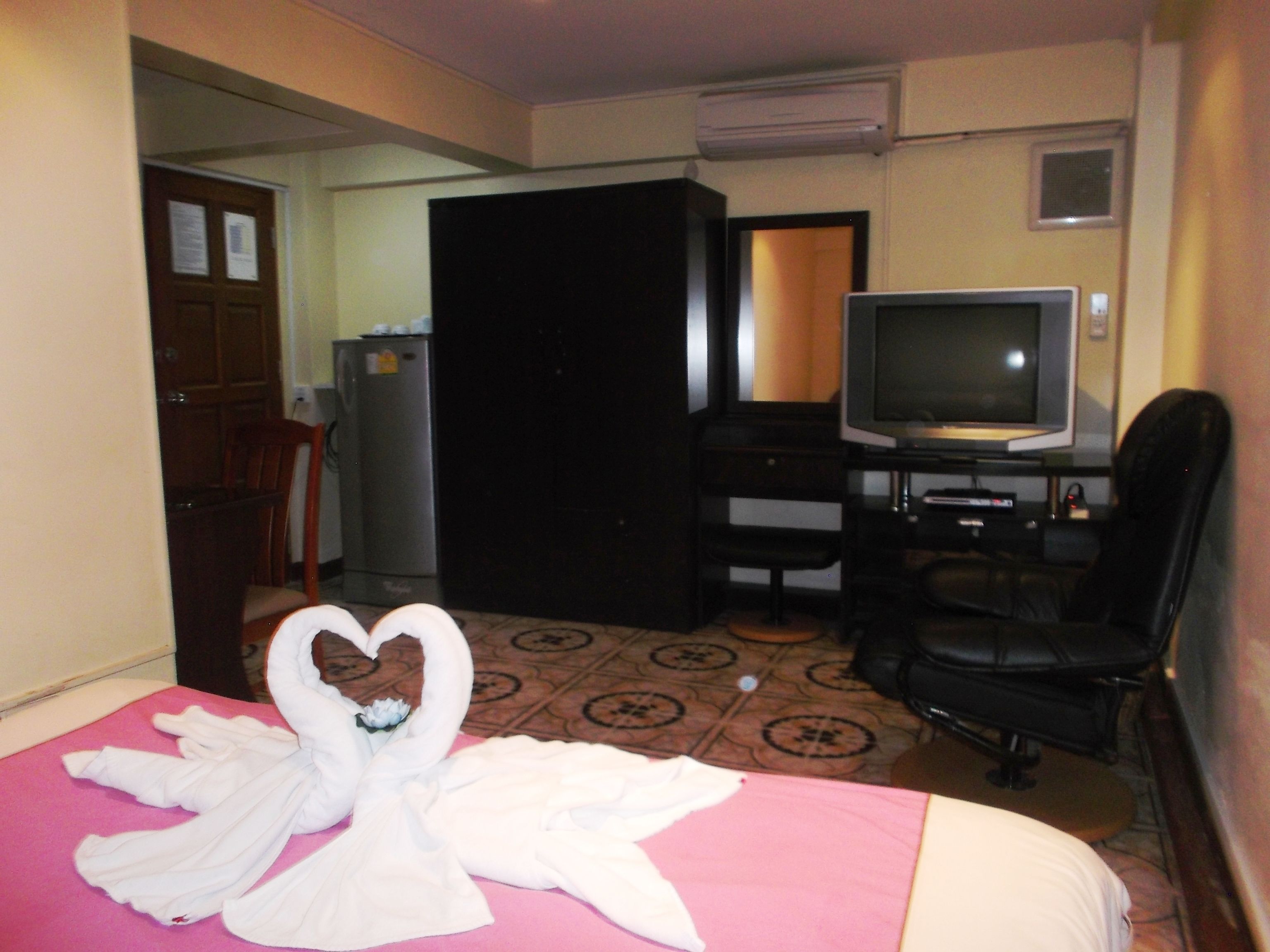 A hotel room with a bed, a desk with a computer, a television, and a refrigerator.