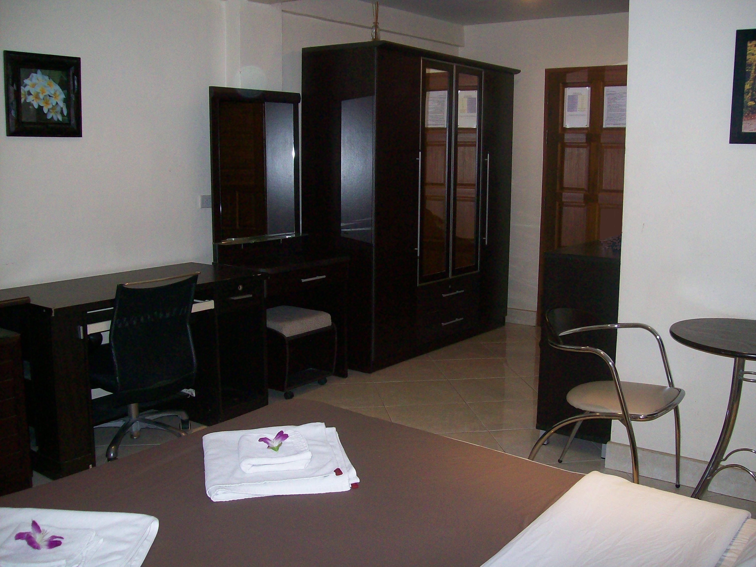 A hotel room with a bed, a desk, a chair, a wardrobe, and a small table.