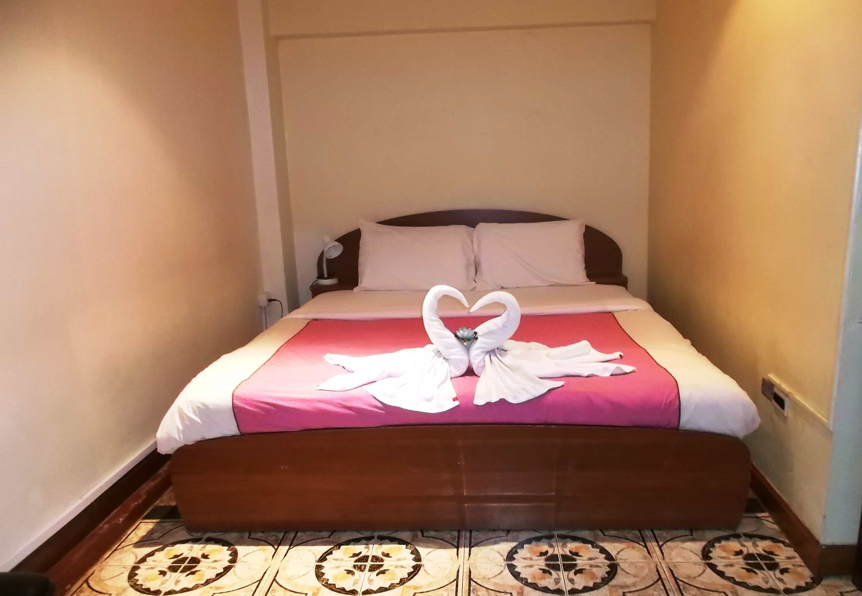 Una habitación de hotel con una cama, cabecero de madera, colcha rosa y un cisne decorativo hecho con toallas sobre la cama.
