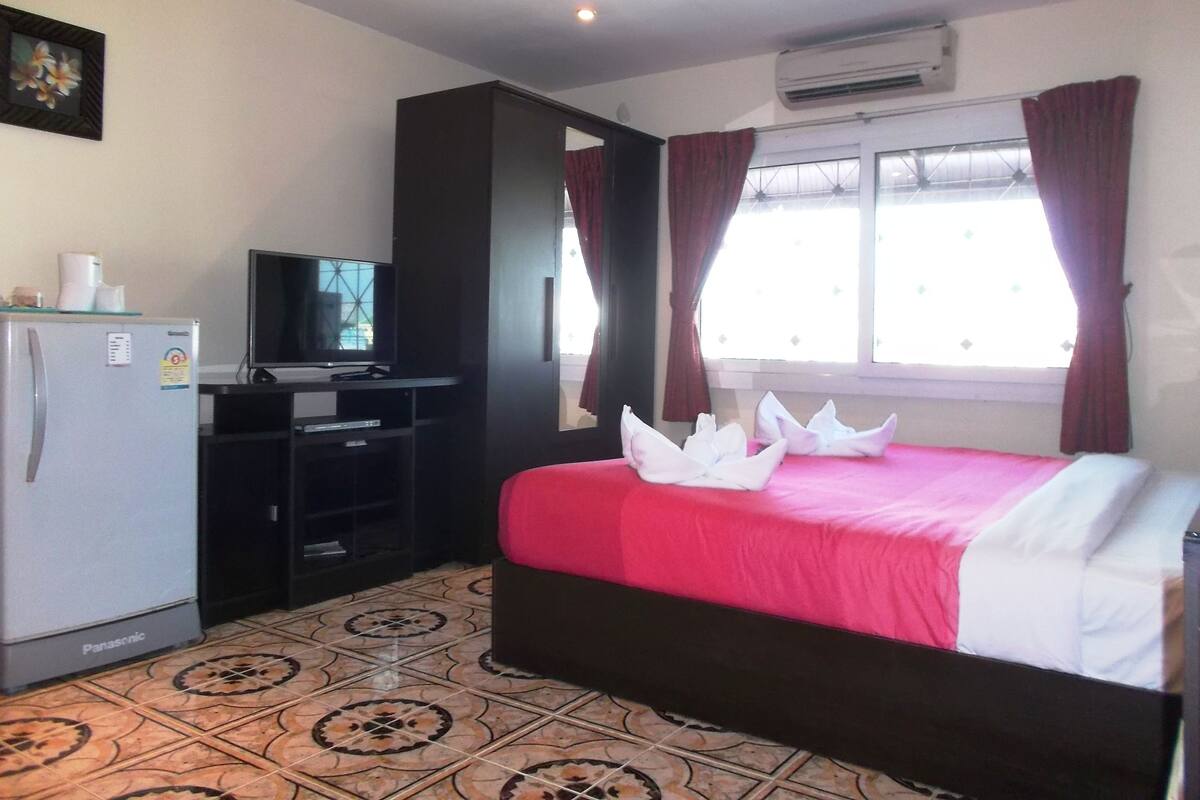 A hotel room with a bed, a television, a refrigerator, and a window with curtains.