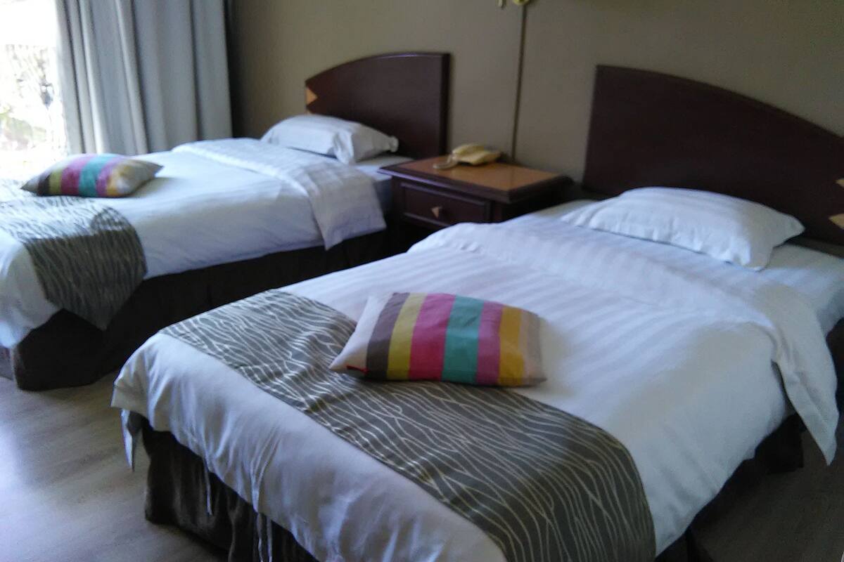 A hotel room with two beds, each with a pillow and a bedside table with a lamp.