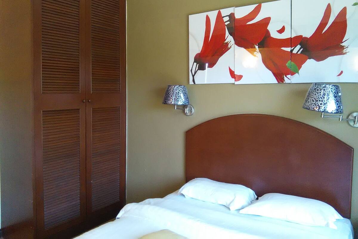A hotel room with a bed, a wooden wardrobe, and a wall-mounted abstract painting.