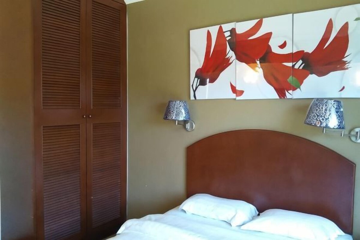 Una camera da letto con testiera in legno, un letto con biancheria bianca, una lampada a parete e un quadro con uccelli rossi.