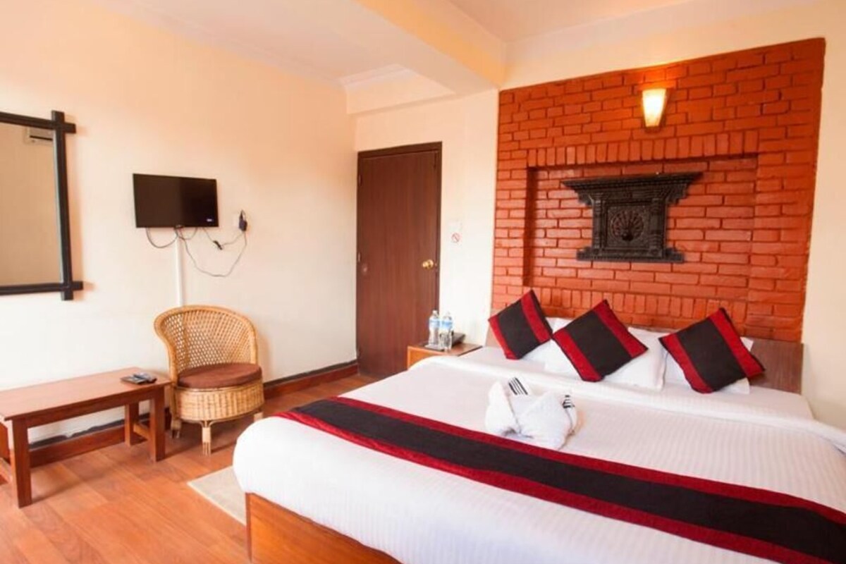 Une chambre d’hôtel avec un grand lit, un téléviseur à écran plat, un fauteuil en osier, une table de chevet en bois et un mur décoratif en briques.