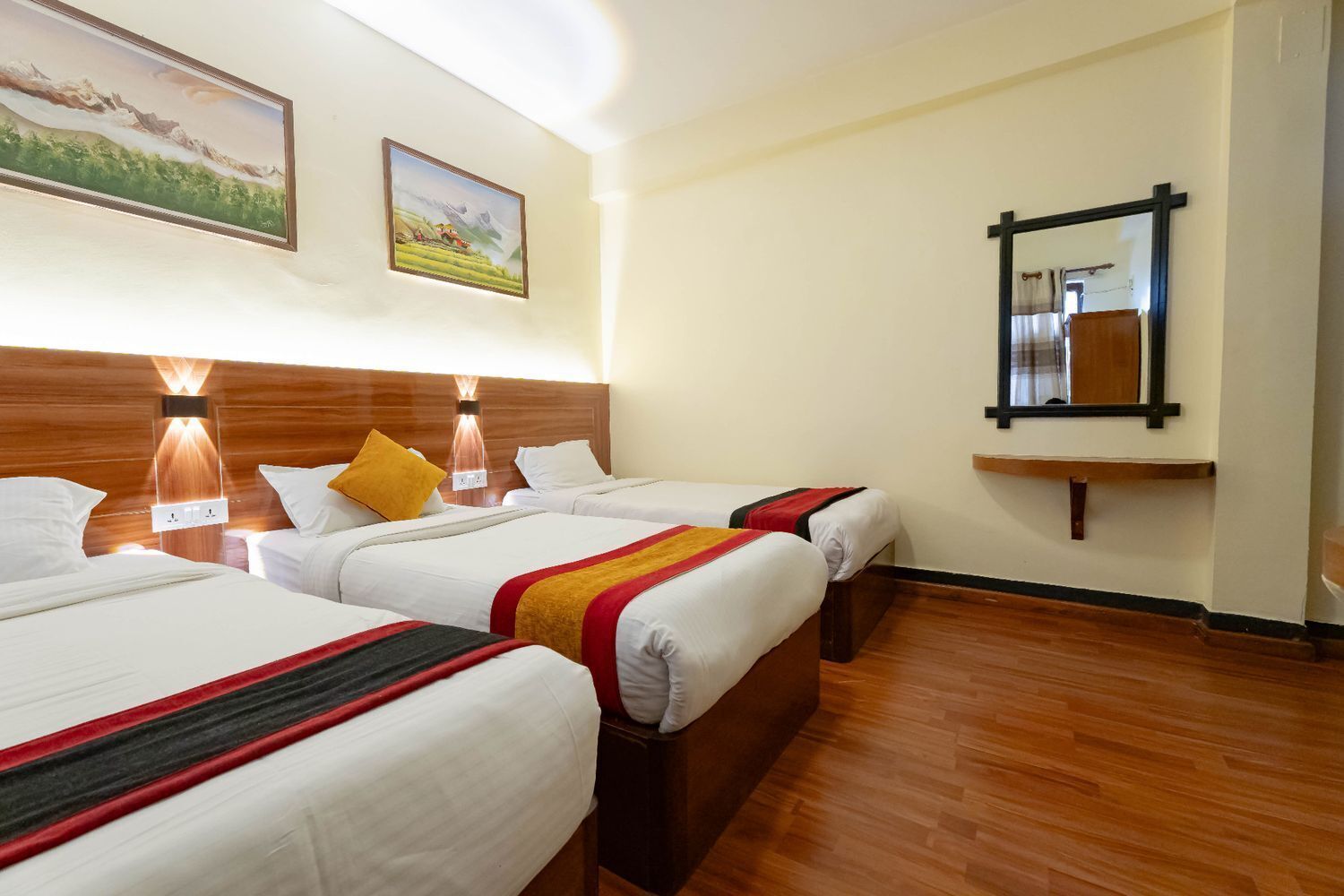 A hotel room with three beds, wooden headboards, and a mirror on the wall.