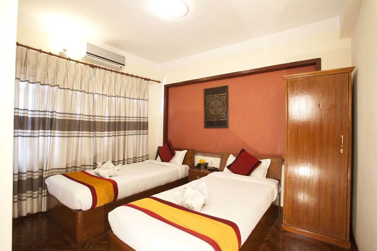 A hotel room with two beds, a wardrobe, and an air conditioning unit.