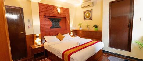 A hotel room with a bed, a nightstand, a wall-mounted air conditioner, a door, and a small rug.