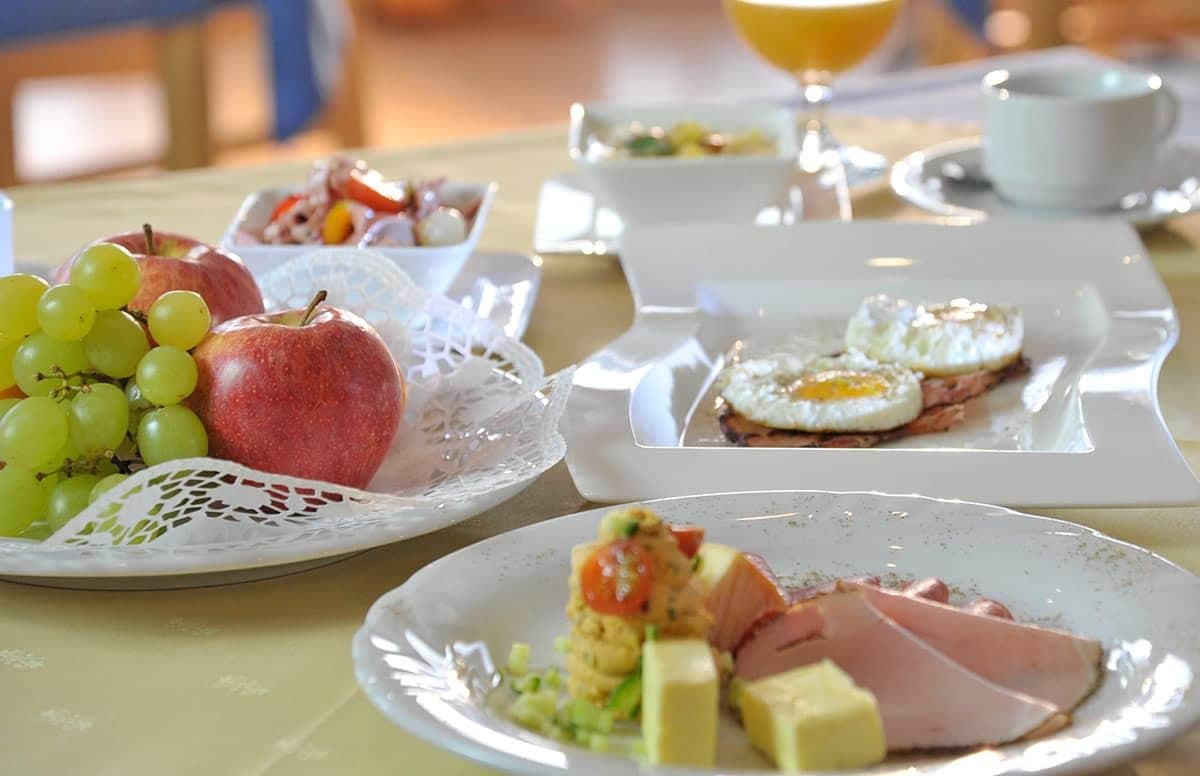 A breakfast setting with plates of food, including eggs, ham, cheese, and fruit.